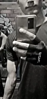 Grayscale gym selfie with defined arm and phone reflection in mirror.