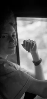 Monochrome portrait of a person looking out the window in soft lighting.