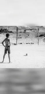 Boy by soccer ball on dusty field, dreaming big.