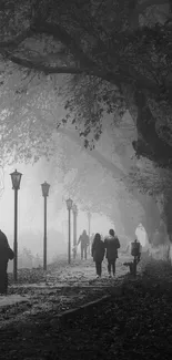 Monochrome foggy forest path with people walking under street lamps.