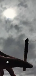 A hand holds a roll against a cloudy sky.