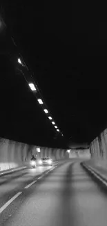 Moody tunnel road with faint car lights in dim black and white setting.