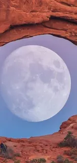 Full moon framed by a red rock arch under a clear sky.