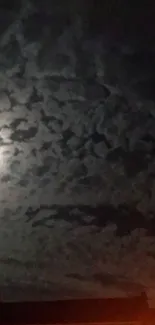 Moonlit cloudy sky with illuminated clouds and faint orange city lights.