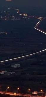 A serene night view of a road winding under a bright, full moon in the night sky.