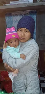 Mother holding baby indoors wearing winter clothing.