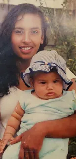 Mother holding baby with a greenery backdrop.