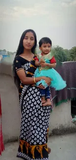 Mother holding child on a balcony, rural setting backdrop.