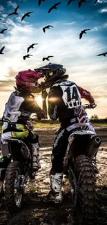 Two motocross riders at sunset under a sky filled with birds.