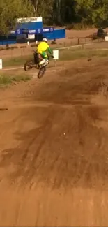 Motocross rider performing jump on a dirt track under a clear sky.