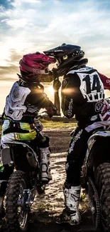 Two motocross riders share a moment at sunset, capturing adventure and camaraderie.