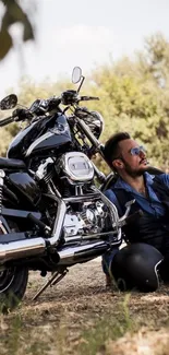 Man resting by motorbike under a tree, embodying outdoor adventure.