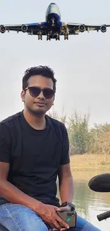 Man on motorbike near lake with airplane overhead.