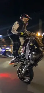 Motorbike stunt at night with rider performing a wheelie.