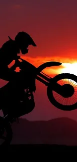 Motorbike performing stunts at sunset with orange sky backdrop.