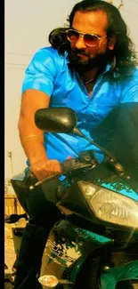 A biker in a blue shirt riding a motorcycle under the sun.