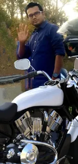 Person next to motorcycles on a scenic road with a green backdrop.