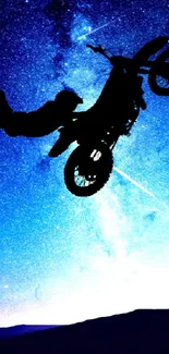 Silhouette of motorcycle stunt against starry blue night sky.