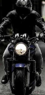 Biker rides through a dark road, helmet on and headlights shining.