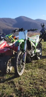 Dirt bikes on a grassy hill with mountains in the background.