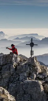 Person on rocky mountain with cross; misty horizon view.