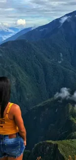 Traveler gazes at verdant mountain view, misty peaks in the background.