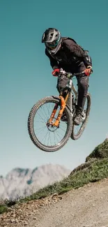 Mountain biker jumps on a scenic outdoor dirt trail against a blue sky.