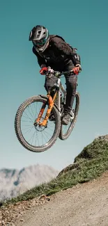 Cyclist jumps on mountain trail under a clear blue sky.