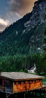 Wooden cabin by a mountain lake with lush green forest.