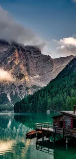 Wallpaper of a tranquil mountain lake with a rustic cabin and lush green forests.