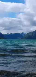 A calm mountain lake with blue water under a cloudy sky with distant hills.