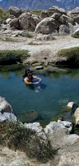 Person enjoying a hot spring in a rocky mountain landscape.