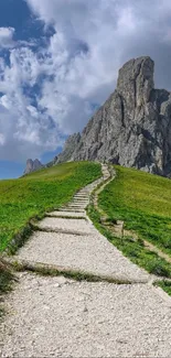 Serene mountain path leading to a rocky peak under a cloudy sky.