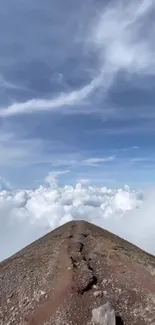 A rocky mountain path leads toward fluffy clouds in a blue sky.