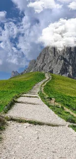 Mountain path under a blue sky with lush greenery and rocky peak.