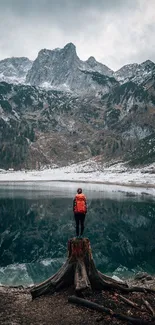 Person with backpack standing by a reflective lake with mountains.