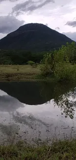 Serene mountain reflection with lush greenery and cloudy skies.