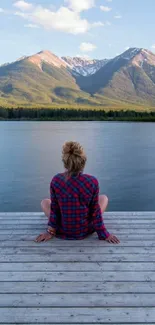 Person sitting on dock facing mountain view under clear blue sky.