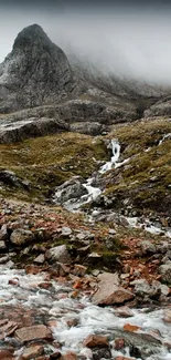 Serene mountain stream flowing under misty skies in a rocky landscape.