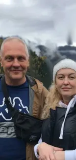 Couple standing in front of misty mountains, wearing casual outdoor clothing.