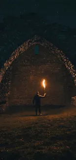 A lone figure holds a torch under a dark archway at night.