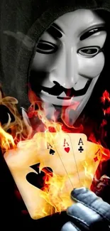 Masked figure holding flaming playing cards in the dark.