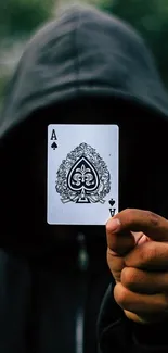 Hooded figure holding Ace of Spades card in mystery-themed wallpaper.