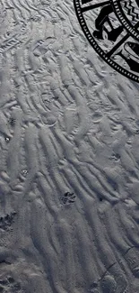 Textured beach sand with zodiac symbols overlay on a mobile wallpaper.