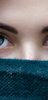 Close-up of green eyes peering over a teal textured scarf.