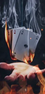 A hand holding flaming, smoking playing cards.