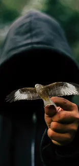 Hooded figure holding a bird in a lush, green forest setting.