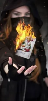 A hooded figure holds a flaming joker card.