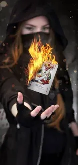 A hooded figure holding a flaming joker card in a dark setting.