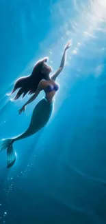 Mermaid swimming upward in deep ocean with beams of sunlight.